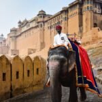 An Indian man riding an elephant near Amber Fort in Jaipur, showcasing vibrant cultural heritage.