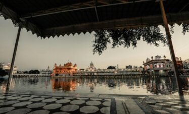 Sidewalk with roof near water with illuminated ancient buildings with fence against gray sky in city street in evening time