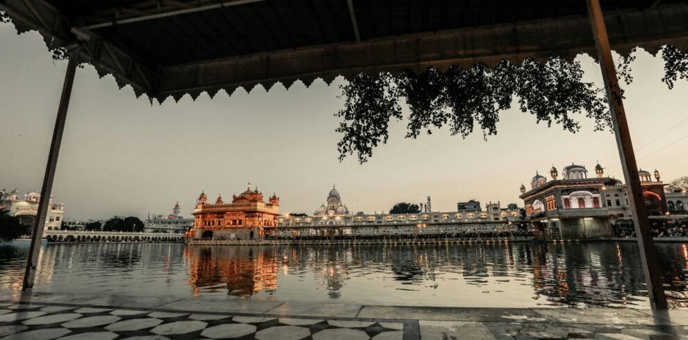 Sidewalk with roof near water with illuminated ancient buildings with fence against gray sky in city street in evening time