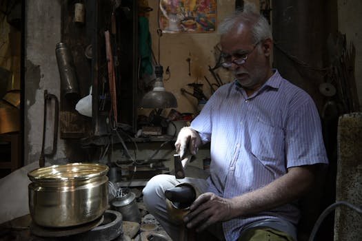 Elderly craftsman at work in an Amritsar workshop, meticulously hammering brass. Captures traditional artisan skills.